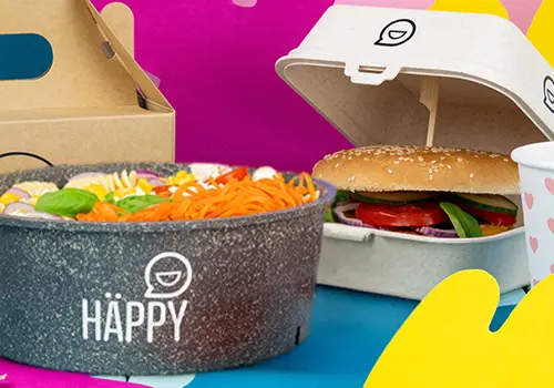 Stos kolorowych misek z napisem "HAPPY BOWL" w różnych wzorach, z osobnym pojemnikiem na jedzenie w tle.
