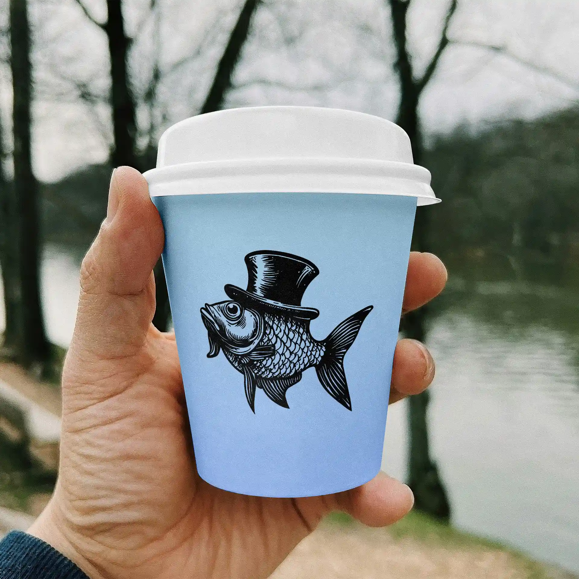 Ręka trzyma jasnoniebieski kubek papierowy z czarną ilustracją ryby w cylindrze, z rozmytym tłem.