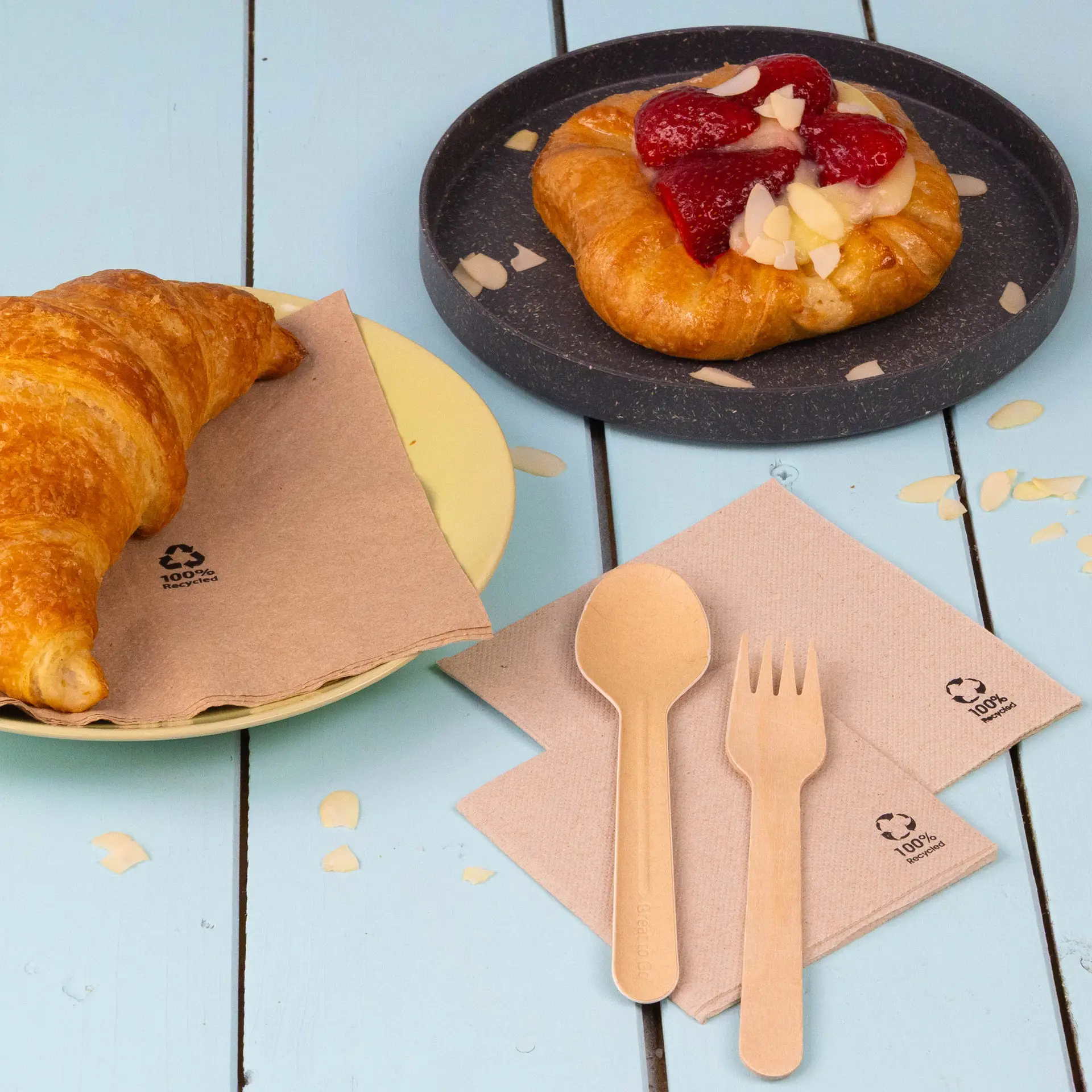 Jedna biała filiżanka kawy z ciastkiem na białym talerzu, otoczona miską malin i serwetkami z papieru recyklingowego.