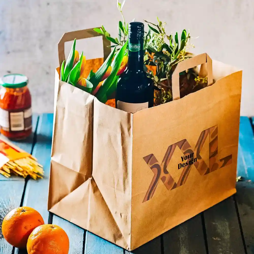 Brązka papierowa torba z uchwytami, zawierająca butelkę wina, kwiaty i słoik, na drewnianej powierzchni z pomarańczami.