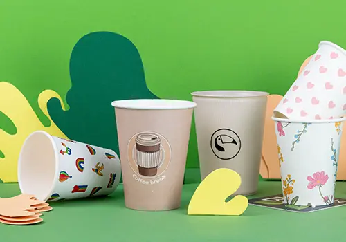 Różne kubki prezentowane na jasnoniebieskiej powierzchni, z różnymi wzorami i etykietami, w tym "Alma & Auer" i "Indie Roasters."