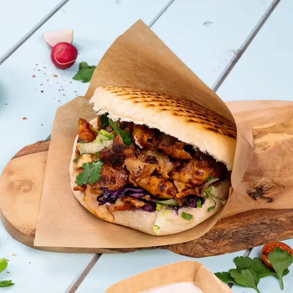 Nadziewana pita z grillowanym kurczakiem, sałatą, purpurową kapustą i kolendrą na drewnianej desce.