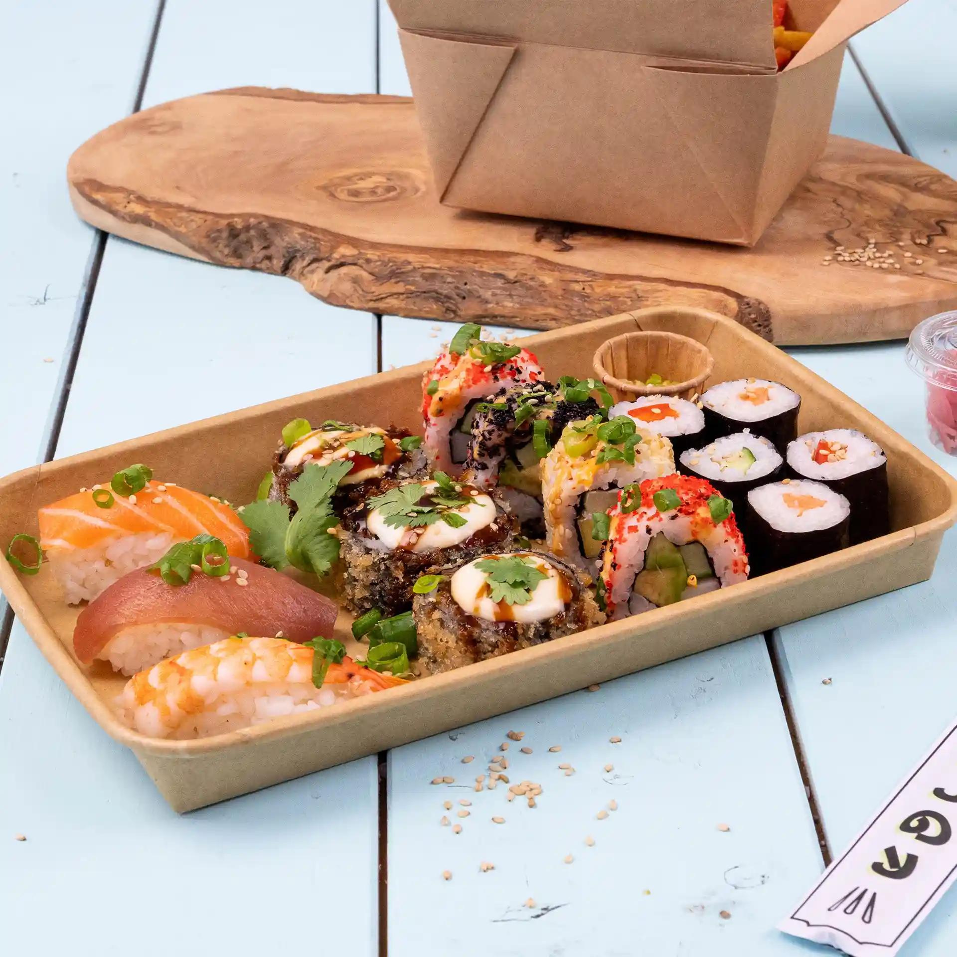Asortyment sushi w brązowym pudełku pokrytym PE, z różnymi rolkami i sashimi na niebieskiej drewnianej powierzchni.