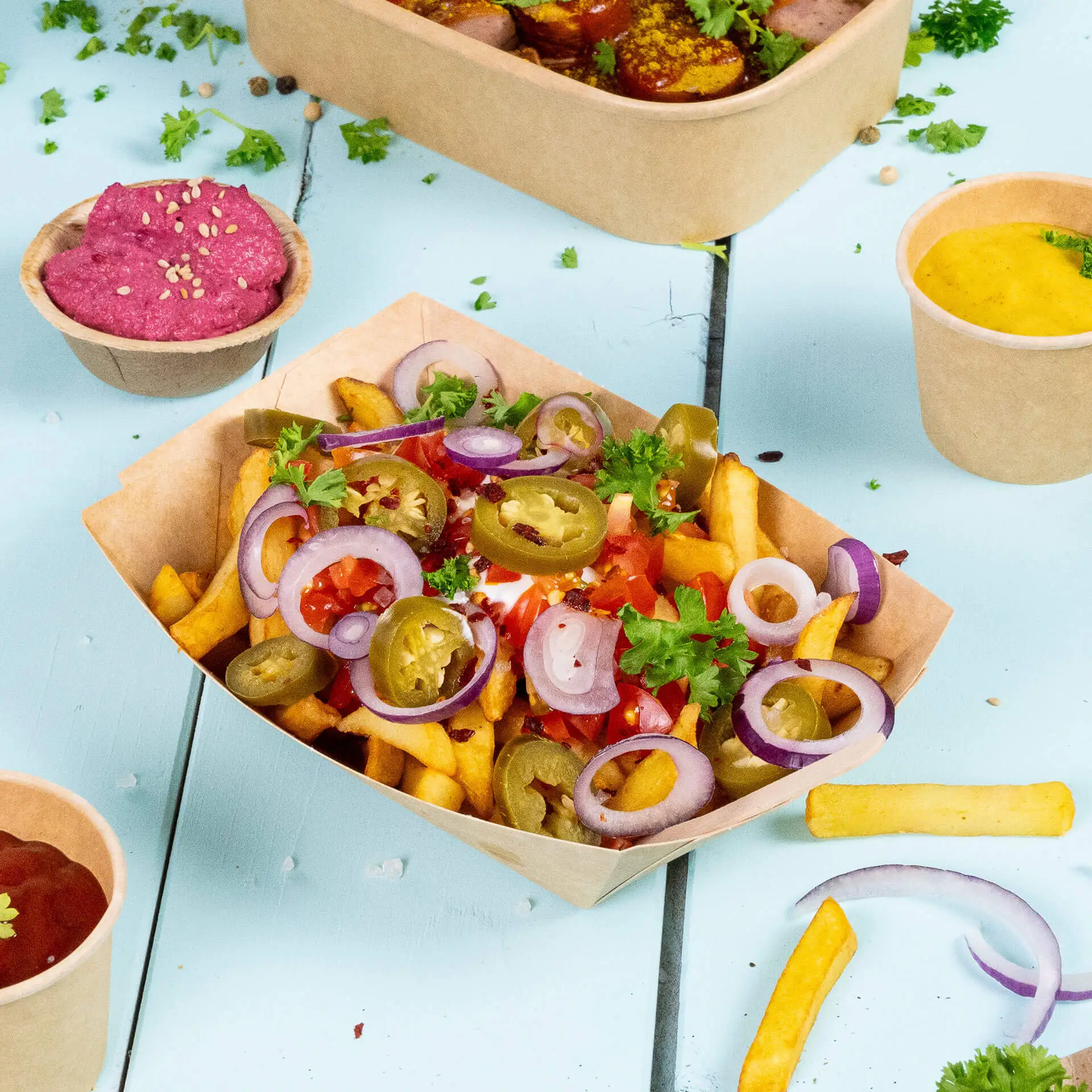 Miseczka odporna na tłuszcz wypełniona frytkami, jalapeños, cebulą i pomidorami; obok różowy dip i kubek sosu.