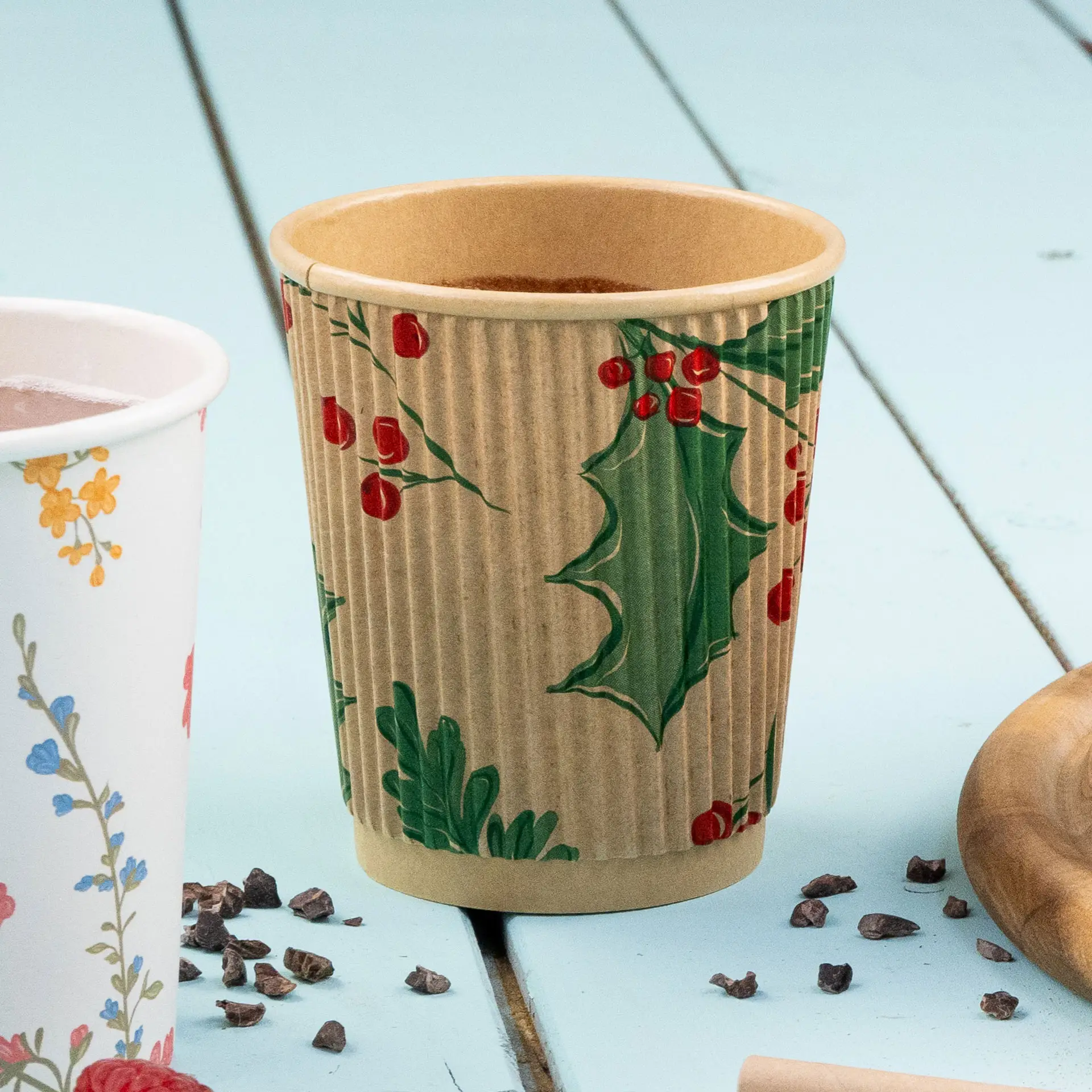 Żłobiony brązowy kubek z nadrukiem ostrokrzewu i jagód; w pobliżu inne kwiatowe kubki. Idealny do gorących i zimnych napojów.