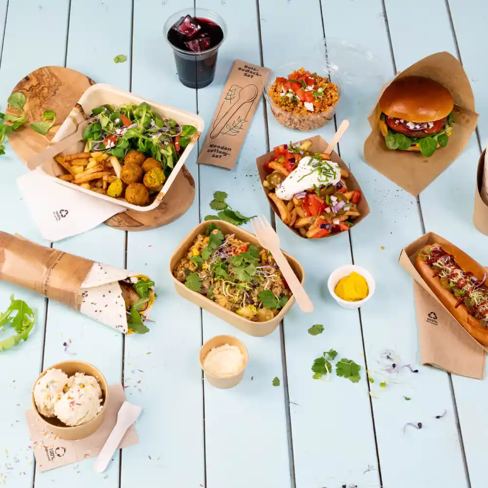 Układ różnych potraw cateringowych na jasnoniebieskim stole, w tym sałatki, burgery, hot dogi i desery. Również napój jest uwzględniony.