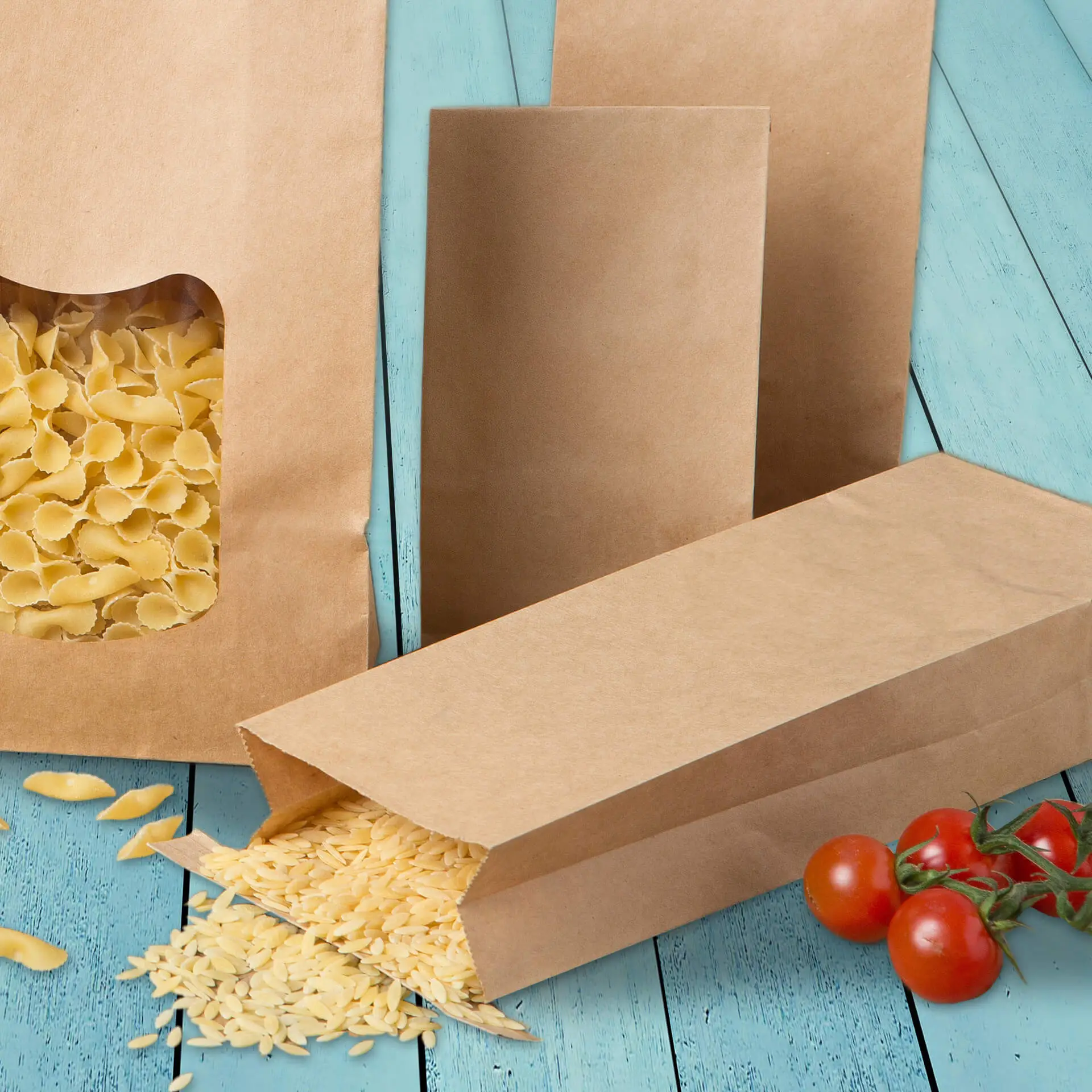 Brązowe papierowe torby z płaskim dnem i oknem, wypełnione makaronem; zawierają rozsypane ziarna i pomidory koktajlowe.