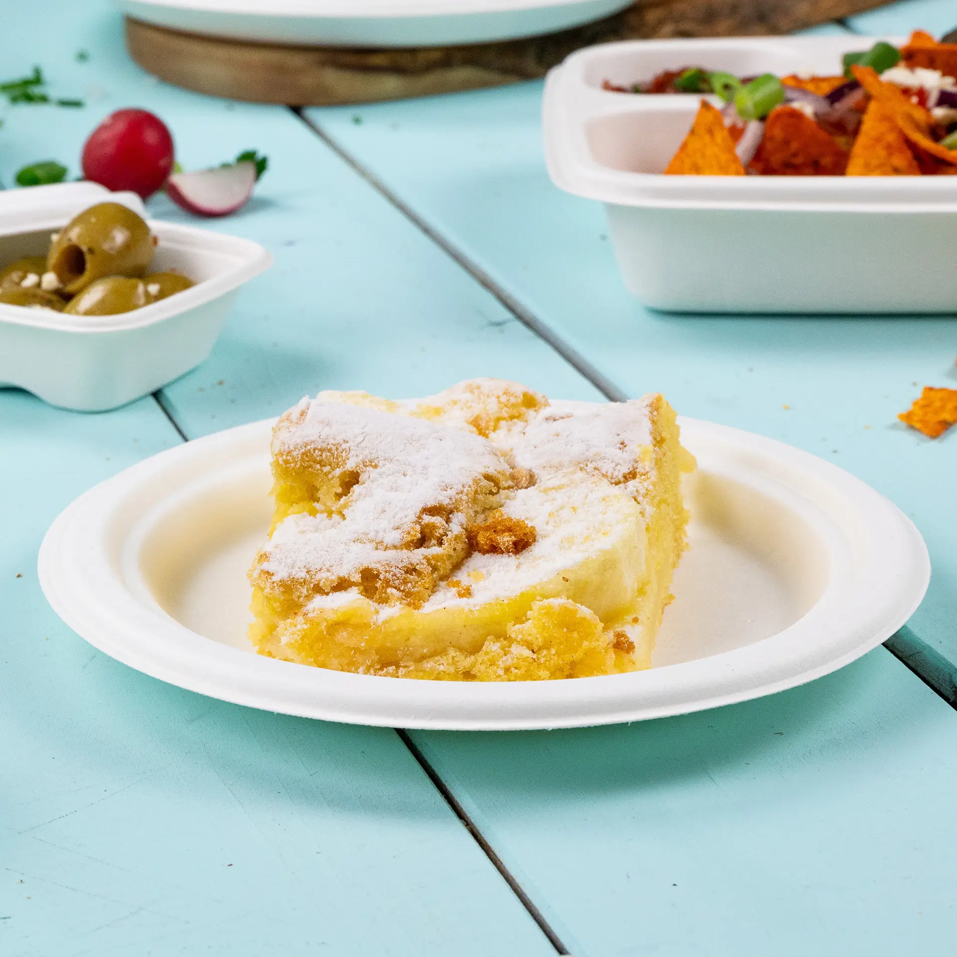 Kawałek ciasta na okrągłym, biodegradowalnym talerzu z trzciny cukrowej, umieszczony na niebieskim drewnianym stole.