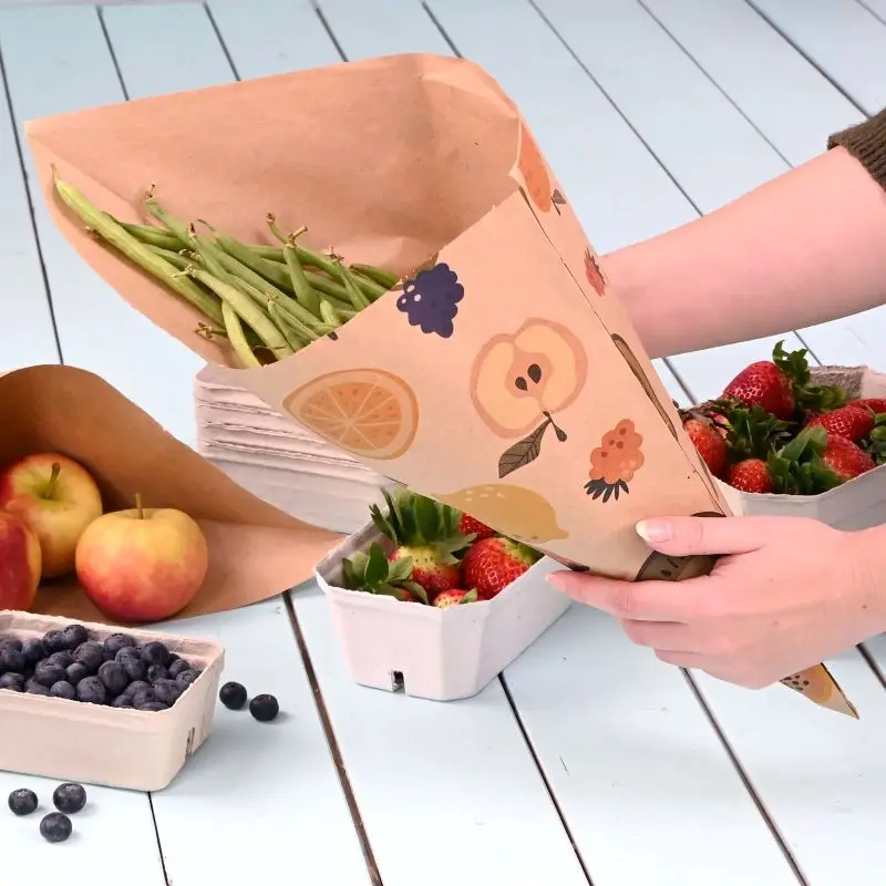 Osoba trzyma kubek z zieloną fasolką, w tle truskawki i jabłka oraz pojemnik z borówkami obok.