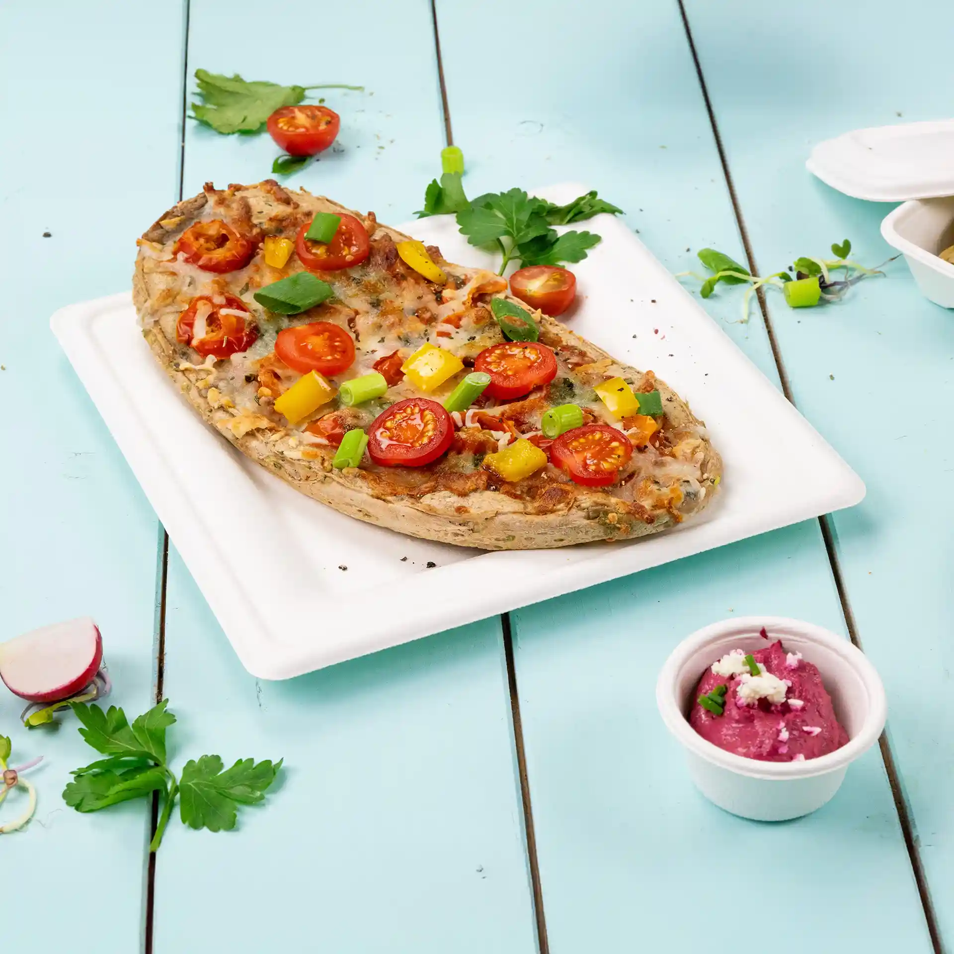Kwadratowy biały talerz z trzciny cukrowej z pizzą z pomidorami, papryką i zieloną cebulką, obok małego kubka z dipem.