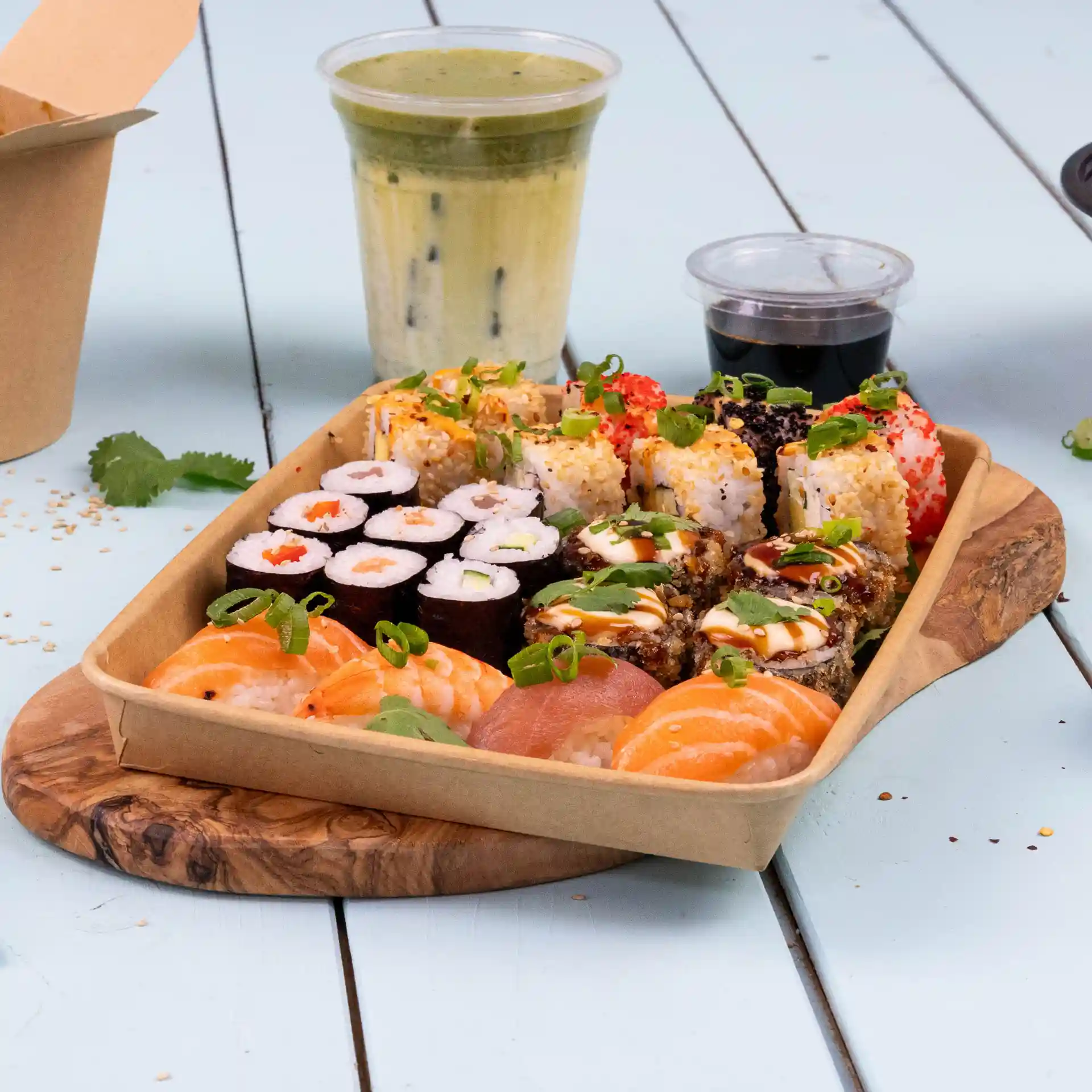 Tacka z różnymi rolkami sushi, w tym krewetkami i łososiem, z napojem i sosem do maczania na drewnianej desce.