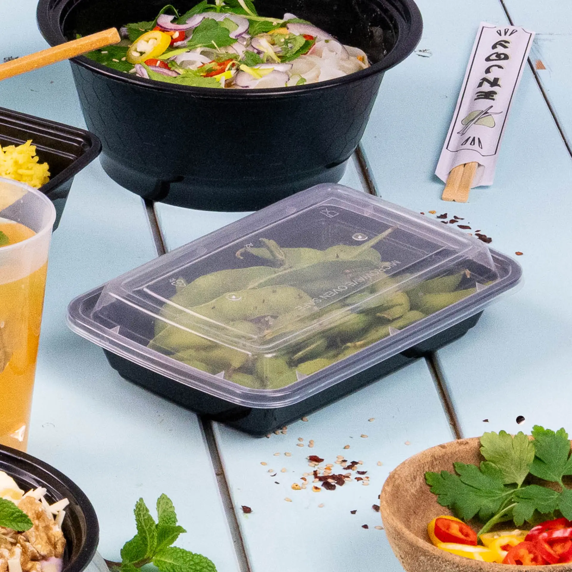 Prostokątny czarny pojemnik do żywności wielokrotnego użytku wypełniony fasolką szparagową; otoczony innymi pojemnikami na posiłki i napojem.