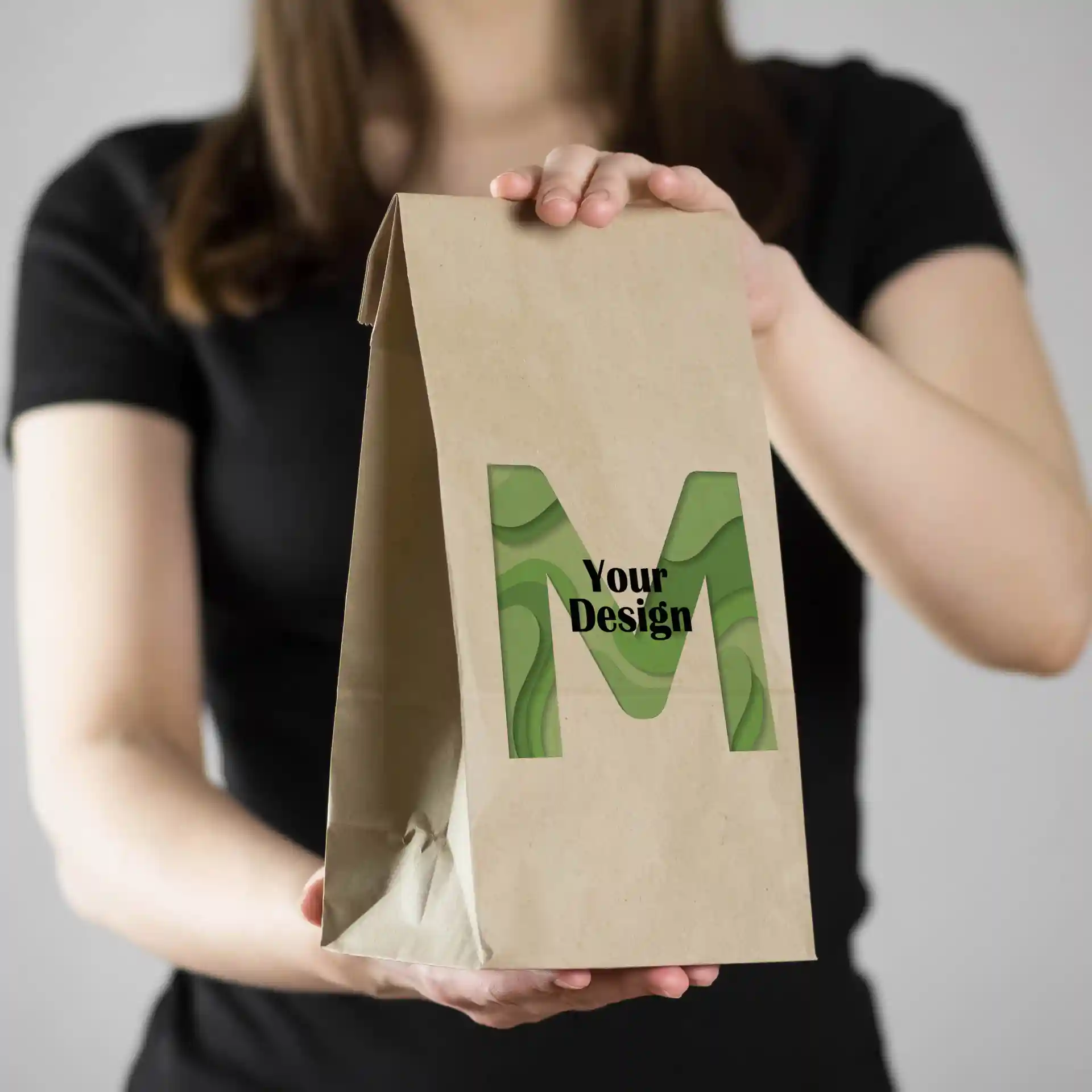 Brązka torba papierowa z zielonym wzorem "M", trzymana przez osobę w czarnej koszulce.