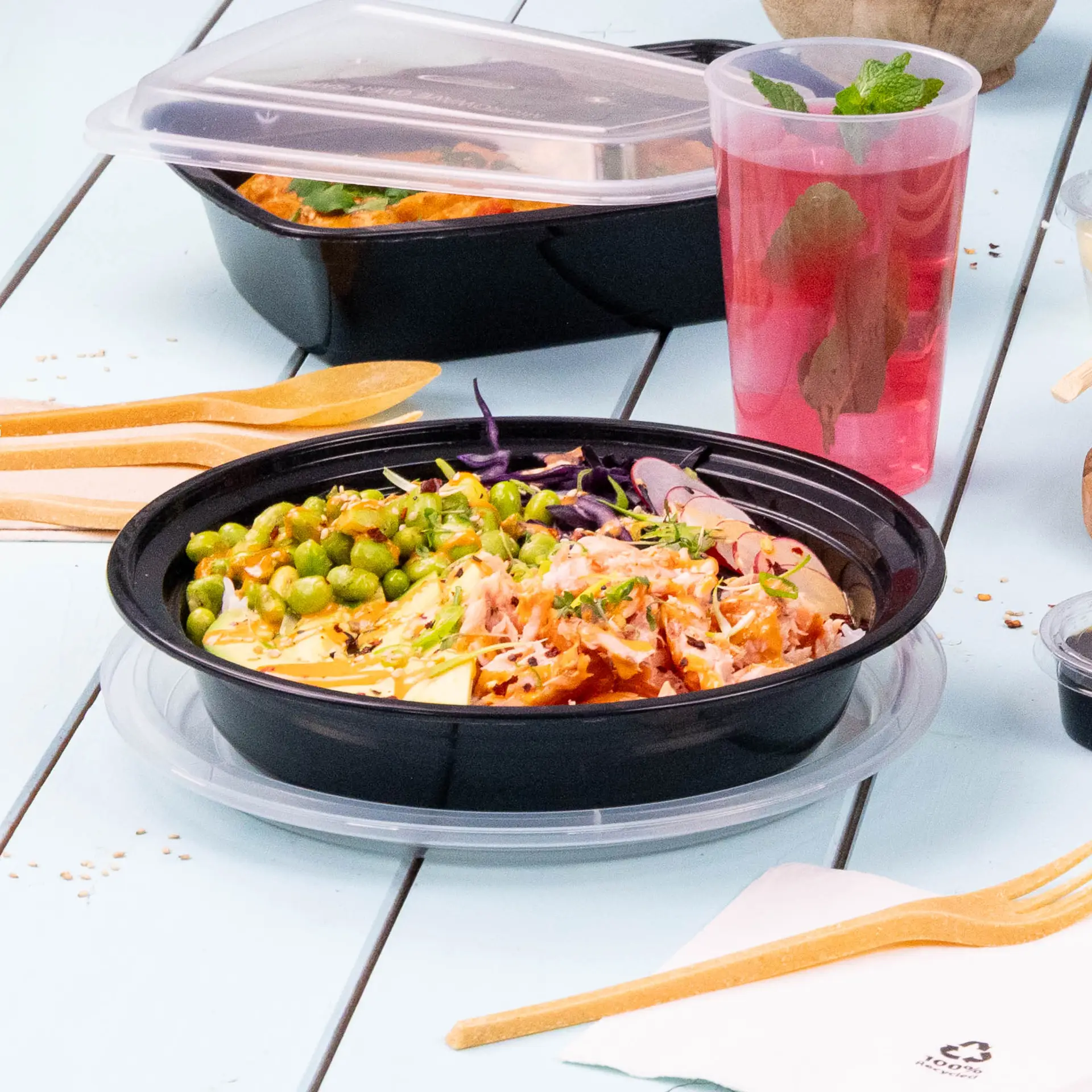 Wielokrotny czarny talerz do dań ciepłych i zimnych, podany z zielonymi grochami, startymi warzywami i napojem; zawiera drewniane sztućce.