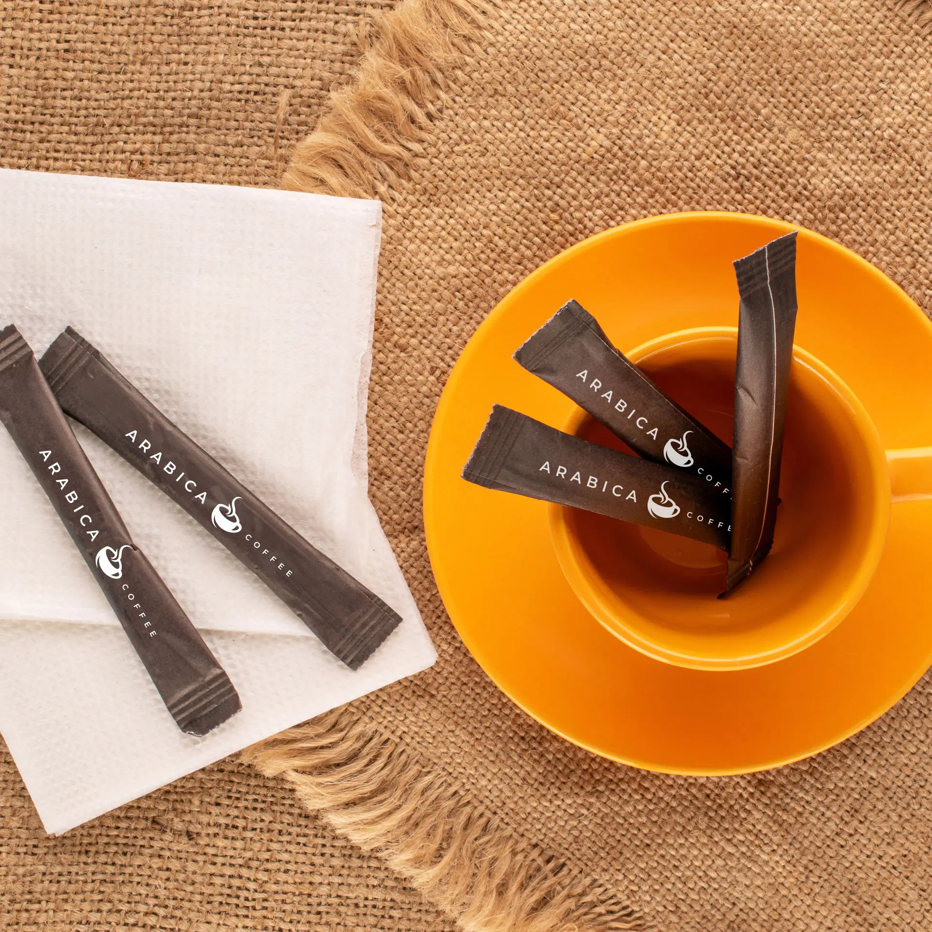 Kilka spersonalizowanych cukierków ze znakiem "Arabica Coffee" leży w pomarańczowej filiżance obok serwetki na teksturowanej powierzchni.