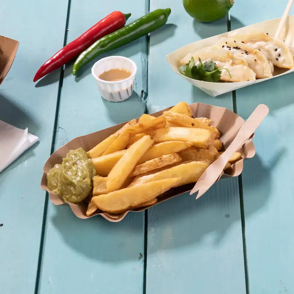Koszyk frytek z zielonym sosem, drewnianymi sztućcami i papryczkami chili na niebieskim drewnianym stole.